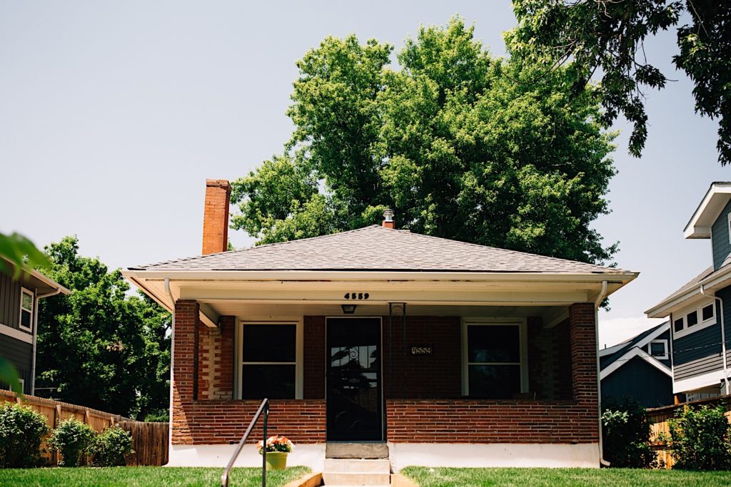 Picture of a the front of a brick house with a giant tree in the background