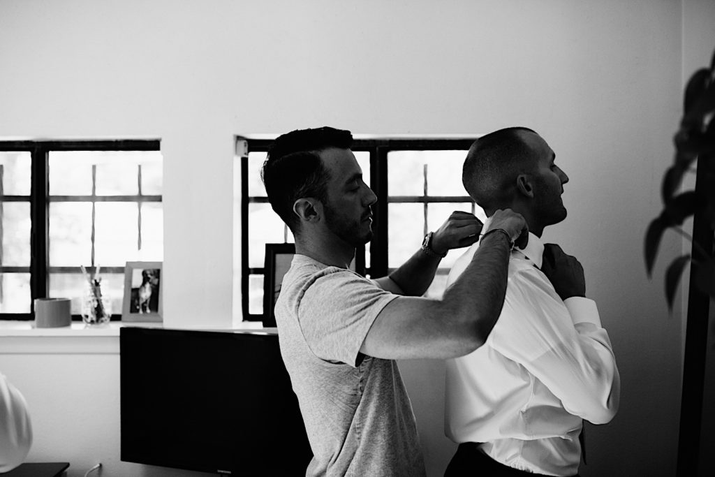 Black and white photo of a man standing behind a groom as he helps to adjust the grooms collar