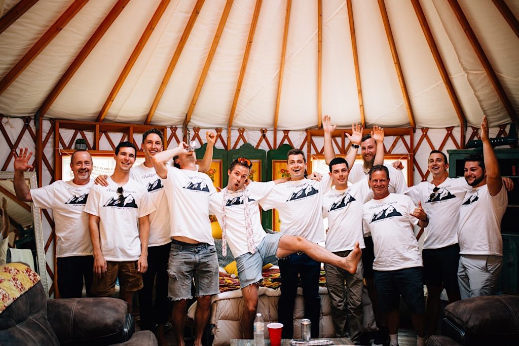 Groom and groomsmen celebrate in front of the camera wearing matching shirts