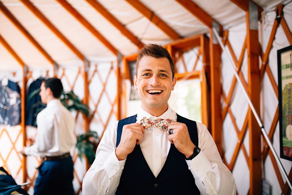 Groom smiles and shows of his flower print bowtie