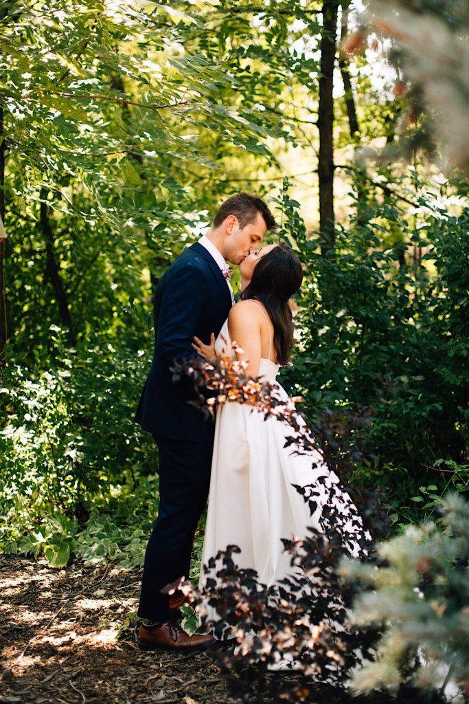 Bride and groom kiss in front of greenery at Planet Bluegrass