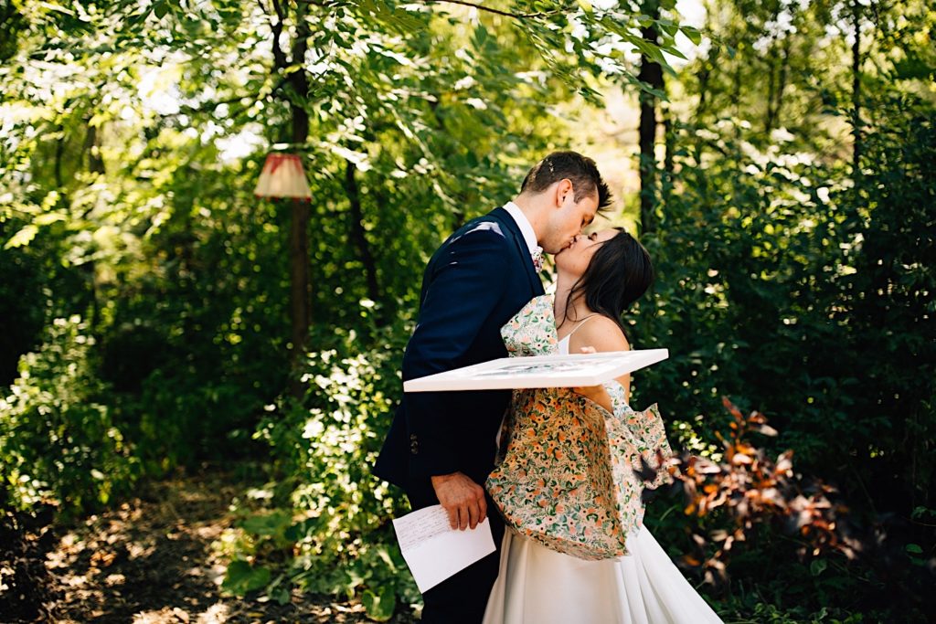 Bride and groom kiss holding gifts they gave each other before their wedding