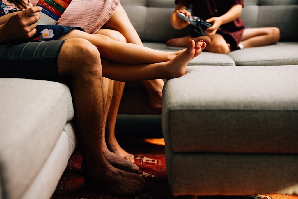 Photo of a family's legs as they sit on a couch together, one set of legs is resting on an ottoman.