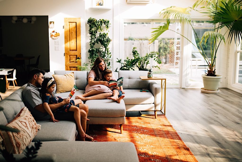 A family sitting on the couch in their house, mother and son sit together and read on one side of the couch while father and daughter sit on the opposite side also reading.