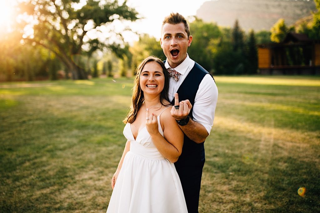 Bride and groom smile and show off their rings to the camera in a field at Planet Bluegrass after their wedding ceremony