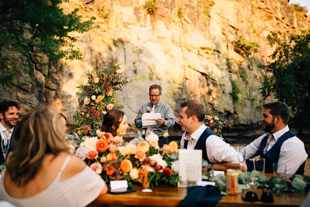 Man gives a speech at a wedding reception at Planet Bluegrass while guests smile and laugh