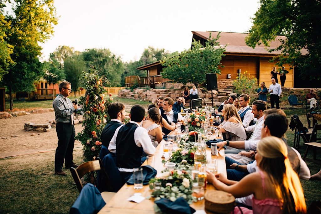 Man gives a speech at a wedding reception at Planet Bluegrass while guests smile and laugh