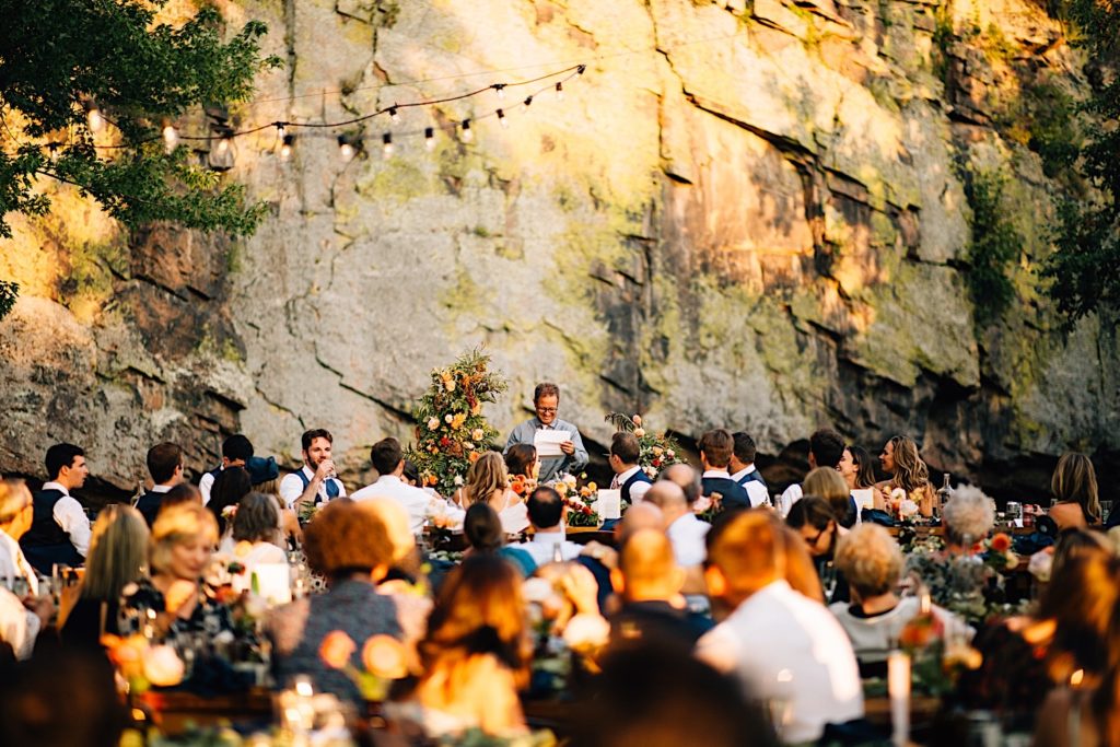 Man smile while giving a speech at a wedding reception at Planet Bluegrass with guests in the foreground