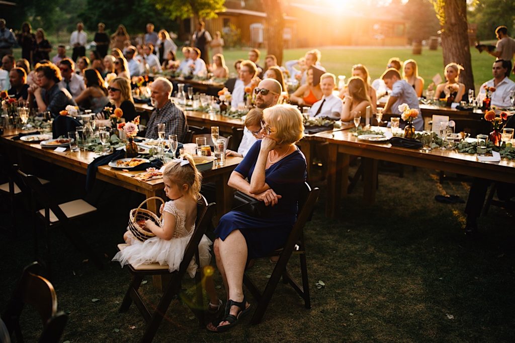 Guests at a wedding reception at Planet Bluegrass watch as someone gives a speech with the sun setting in the background