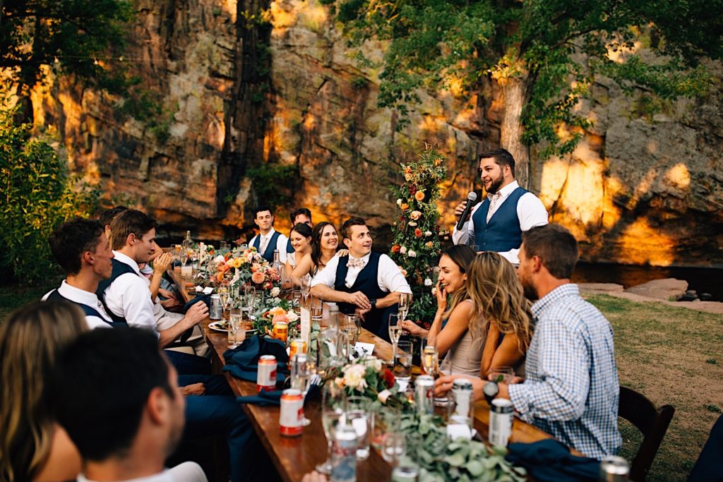 Groomsmen gives a speech at a wedding reception at Planet Bluegrass standing next to the head table