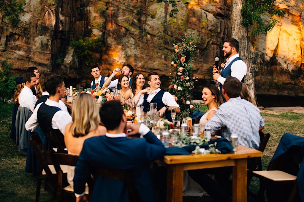 Groomsmen gives a speech at a wedding reception at Planet Bluegrass standing next to the head table