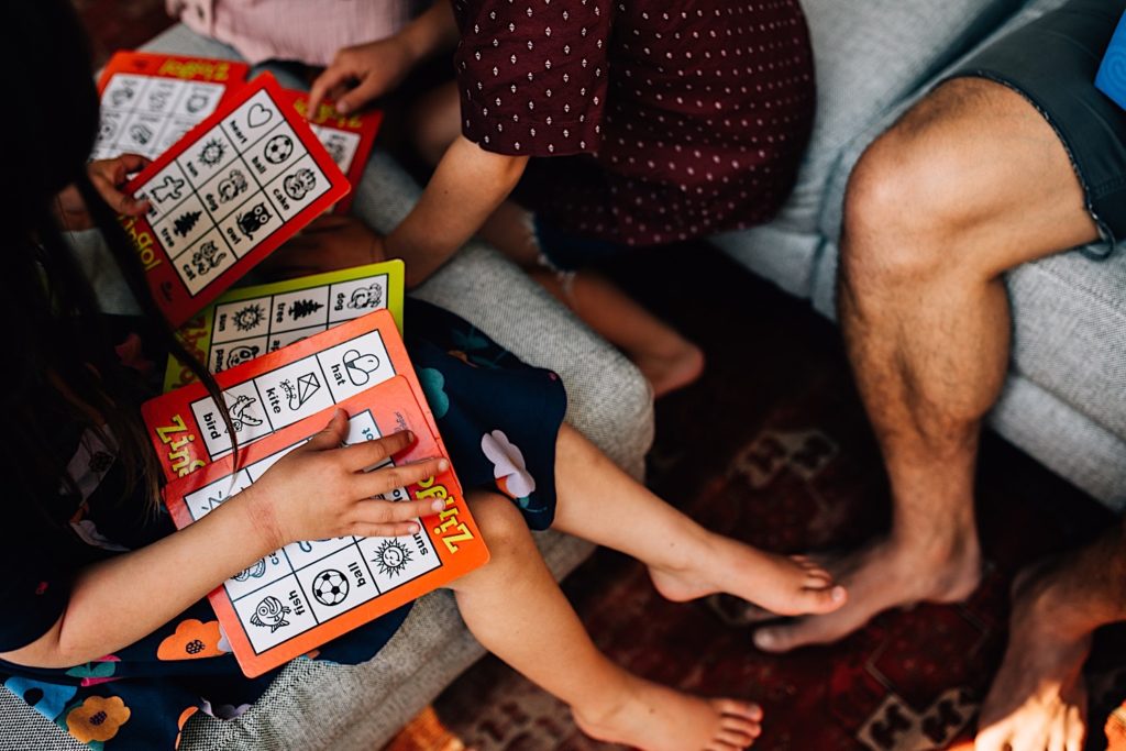 Child sitting on an ottoman holding multiple "Zingo" boards while the rest of her family sits on the couch.