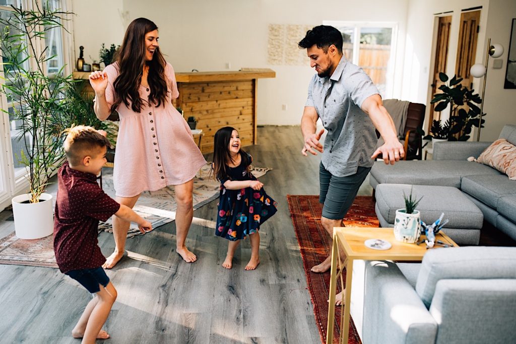 A family dance together in their home's living room, the mother son and daughter all smile and laugh as the dad attempts to floss.