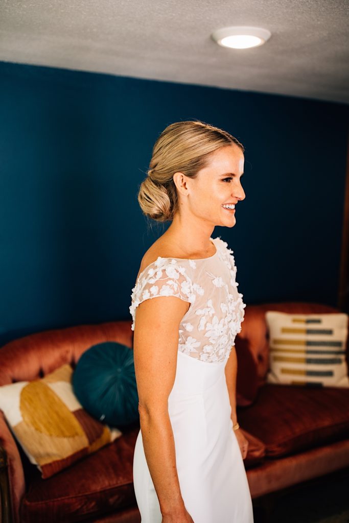 Bride stands smiling at her bridesmaids in her wedding dress while standing in the getting ready space at River Bend in Lyons Colorado