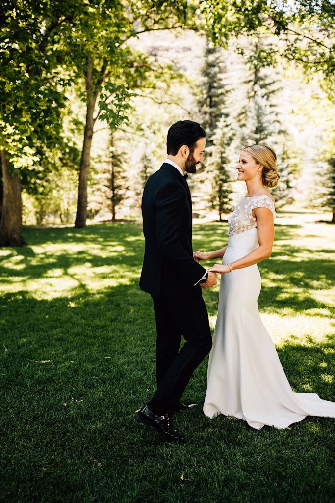 Bride and groom stand amongst trees at their wedding venue, River Bend, in Lyons Colorado