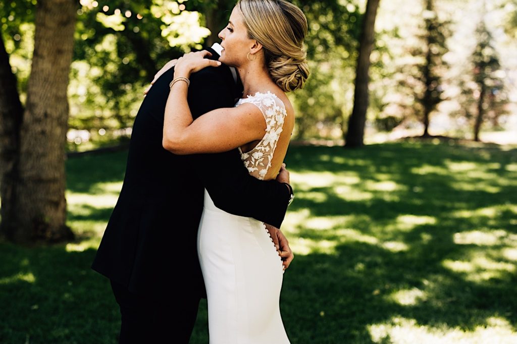 Bride and groom embrace while standing in amongst the trees at their venue in Lyons Colorado