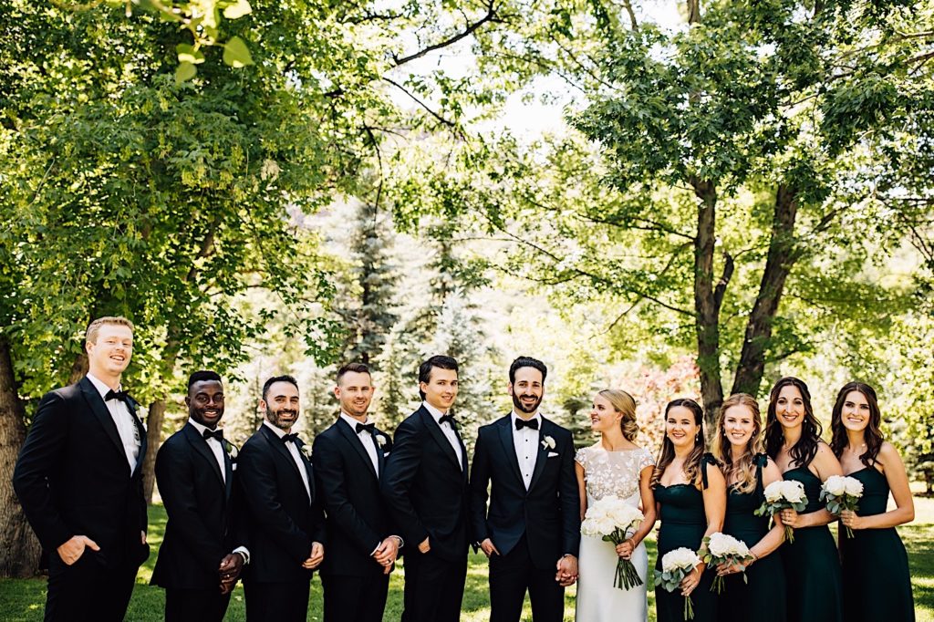 the wedding party stands with the bride and groom.  The wedding party is dressed in all black along with the groom while the bride wears white.