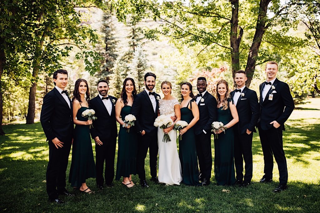 The wedding party stands together for a photo.  The bridesmaids hold white bouquets.