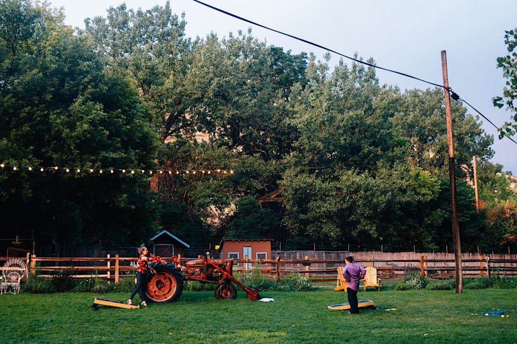 Two people play bags in front of a tractor during cocktail hour at a wedding located just outside of Denver Colorado