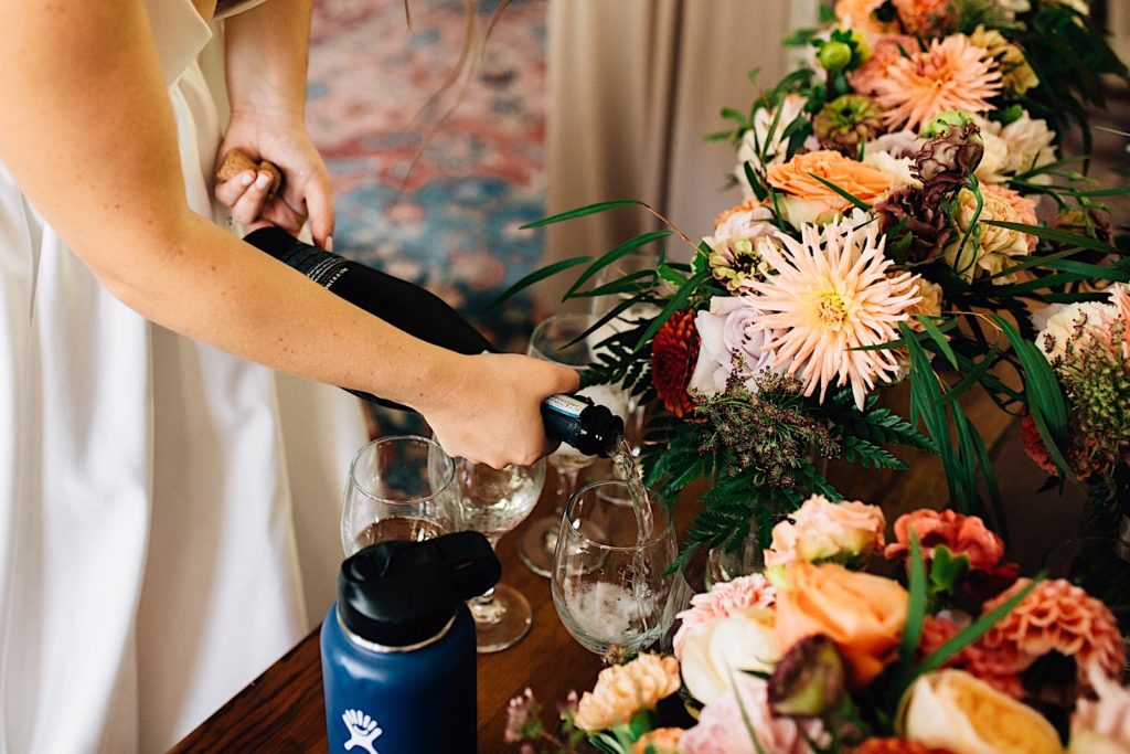Bride pouring champagne into glasses next to bouquets of flowers