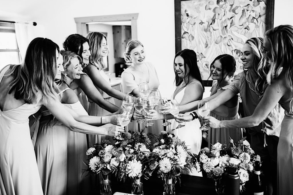 Black and white photo of bride and bridesmaids toasting over bouquets of flowers