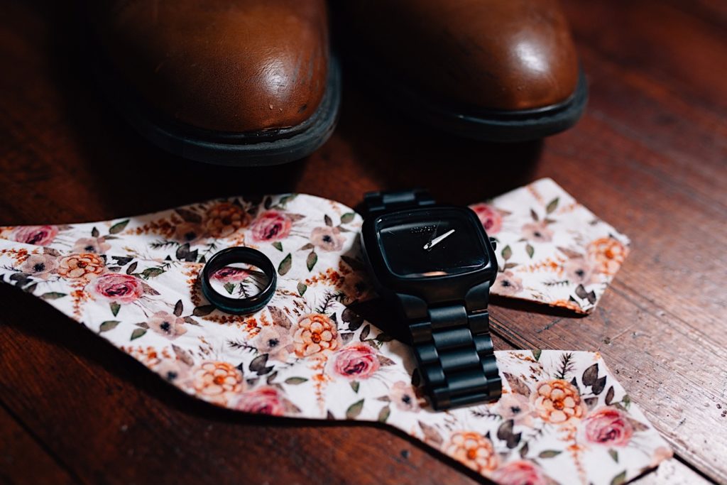 Close up of a wedding ring, watch, flower bowtie and brown dress shoes