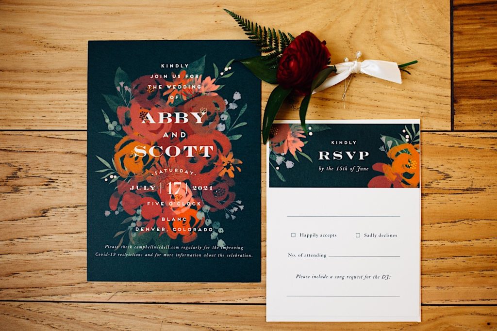 Photo of a wedding invite for Abby and Scott, an RSVP, and a rose all laying on wood