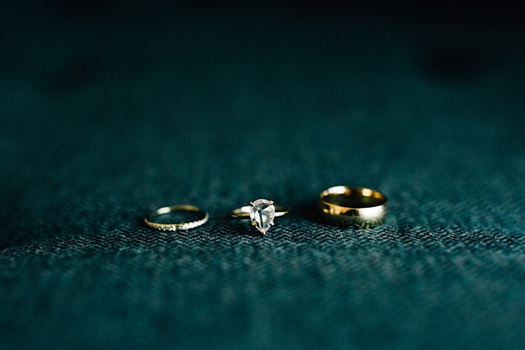 An engagement ring and two wedding rings on a dark teal fabric surface