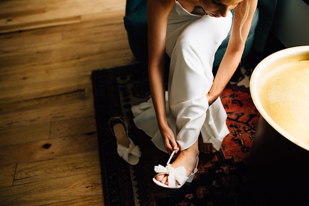 A bride sits and puts on her shoes while wearing her wedding dress
