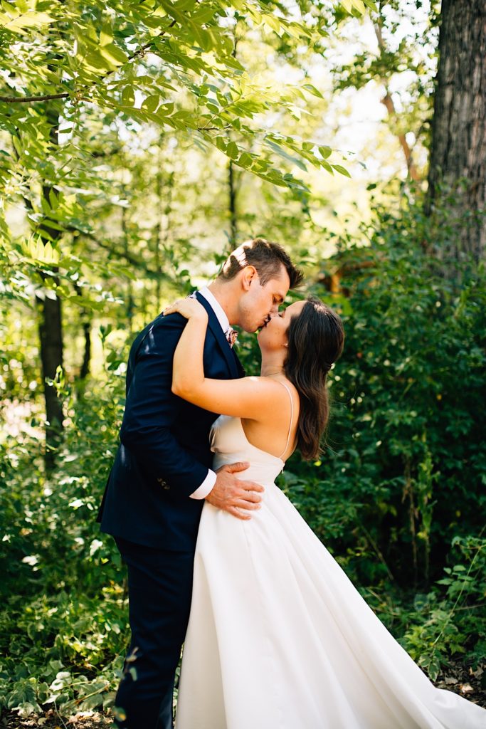 Bride and groom kiss in front of greenery at Planet Bluegrass