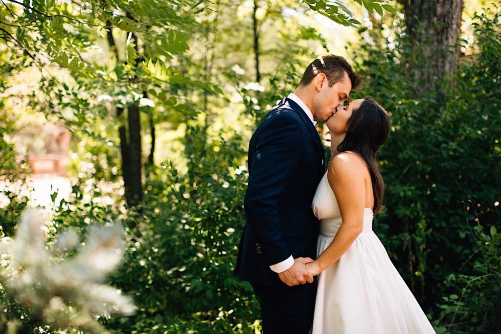 Bride and groom kiss in front of greenery at Planet Bluegrass