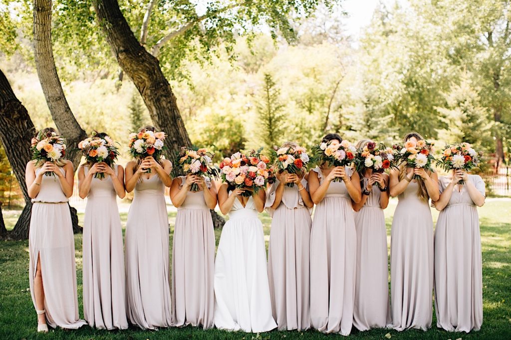 Bride and bridesmaids pose at Planet Bluegrass while holding flower bouquets in front of their faces