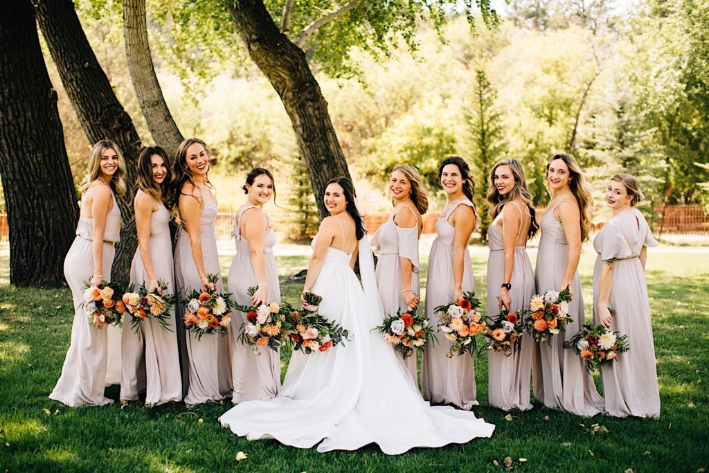 Bride and bridesmaids pose facing away from the camera at Planet Bluegrass while holding flower bouquets