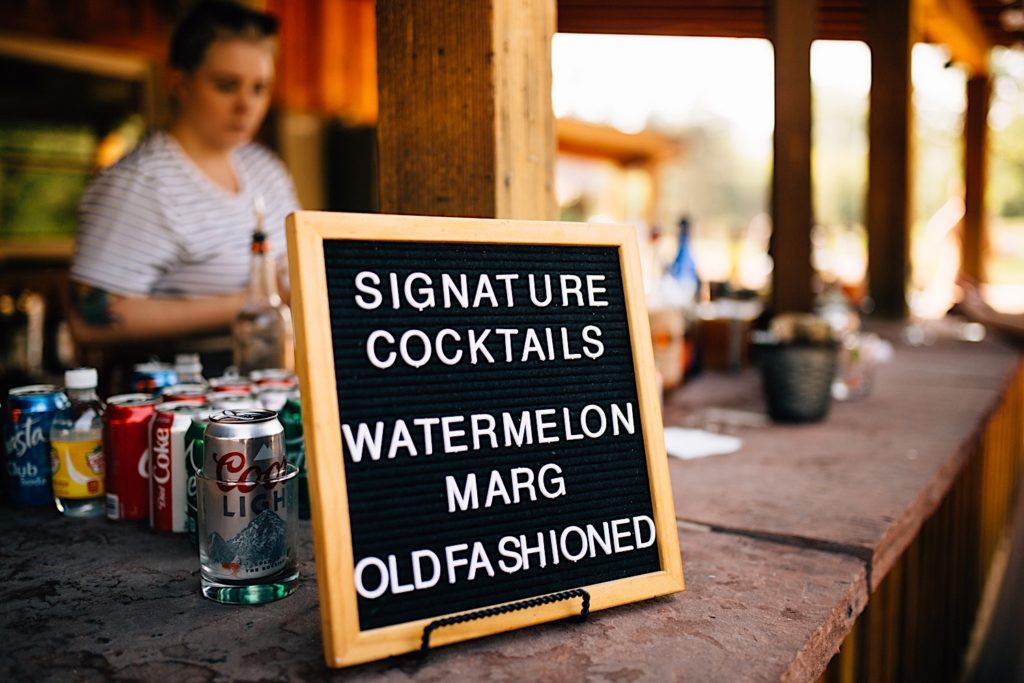 A sign at a bar reads " Signature Cocktails. Watermelon Marg, Old Fashioned"
