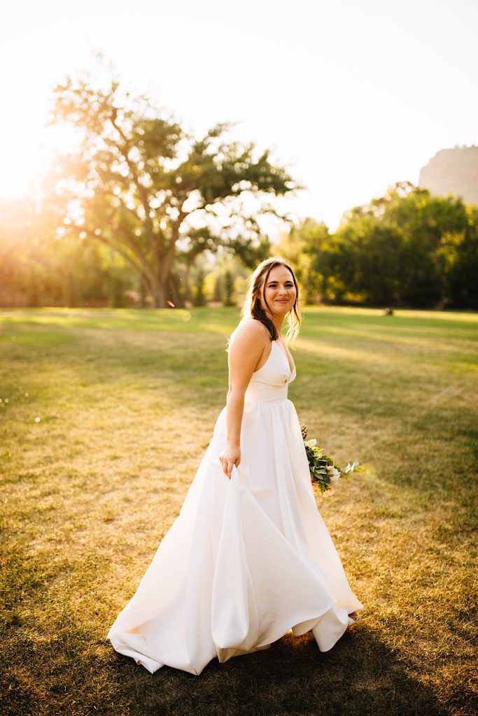 Bride smiles and stands in a field while holding a bouquet at Planet Bluegrass