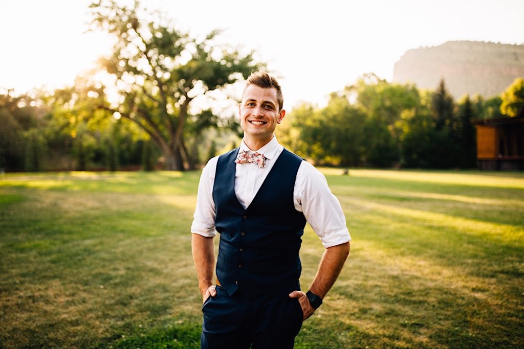 Groom smiles and has his hands in his pockets while standing in a field at Planet Bluegrass