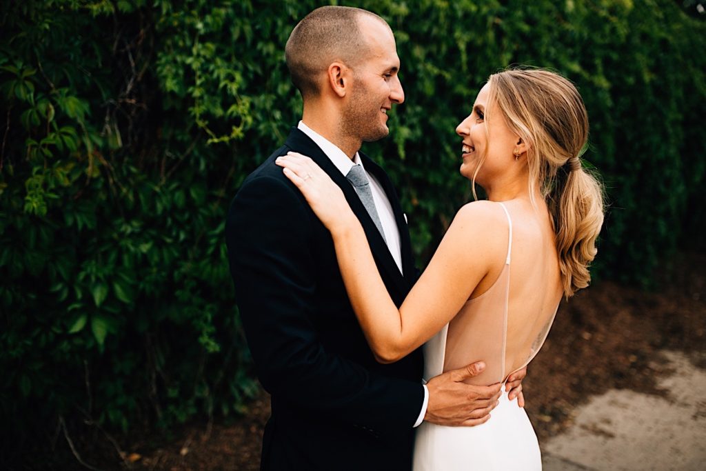 Bride and a groom hold one another and smile at each other wearing their wedding attire
