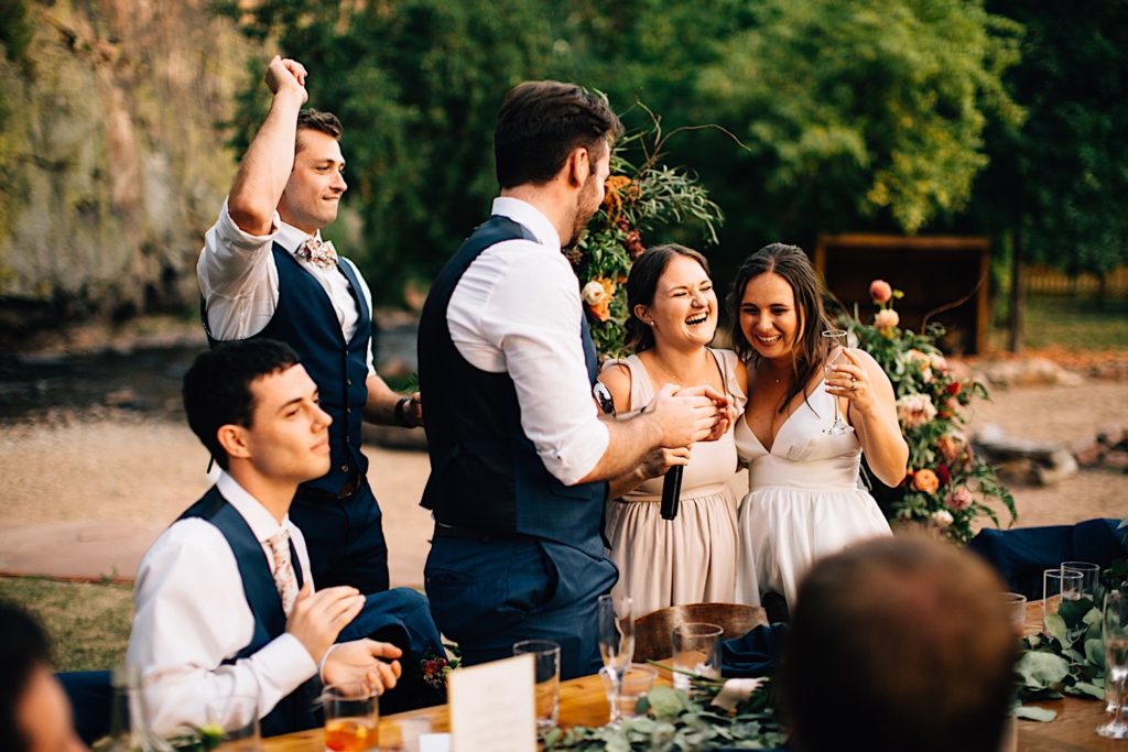 Bride, groom and wedding party stand and laugh together during wedding reception speeches