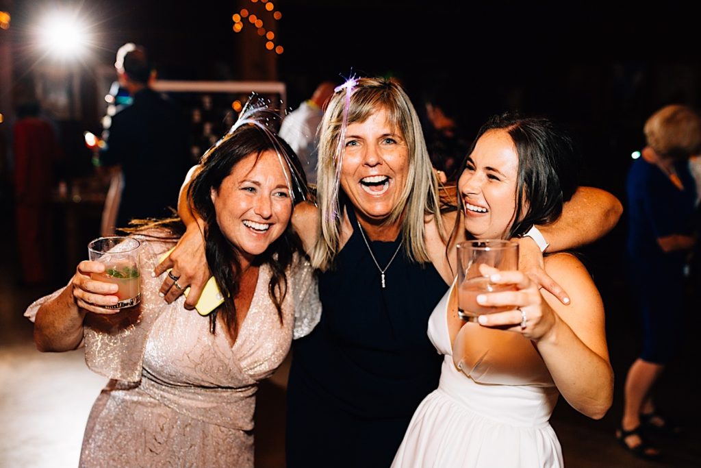 Bride and guests hug and smile while holding drinks during their wedding reception