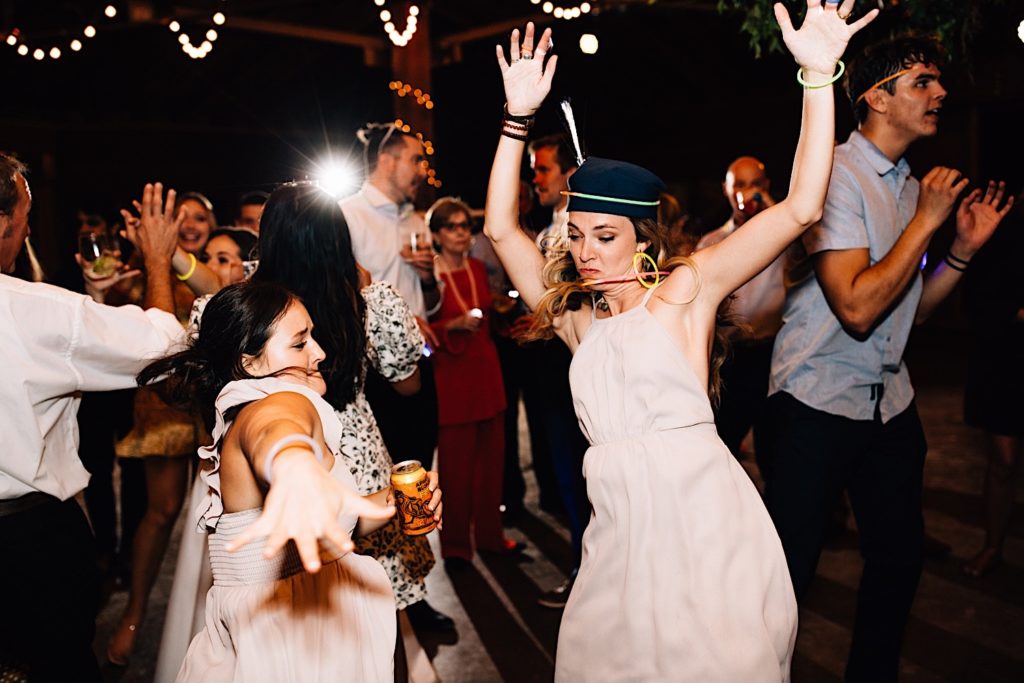 Bride and guests dance on the dance floor during wedding reception wearing glow necklaces