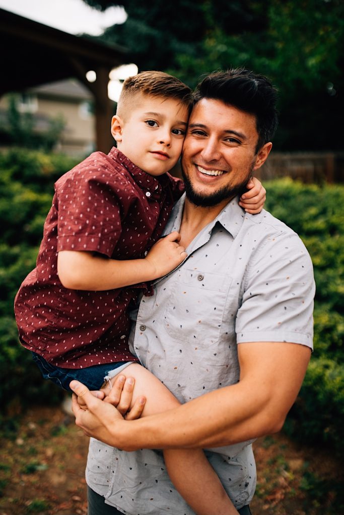 A father holds his son while they both smile at the camera