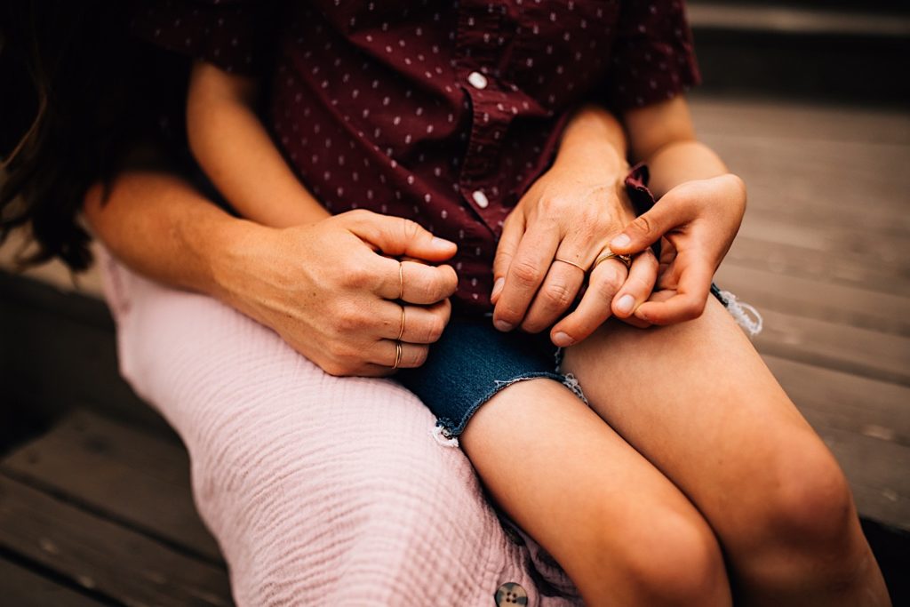 A child sitting on his mothers lap as they hold hands, only their torsos and legs are visible