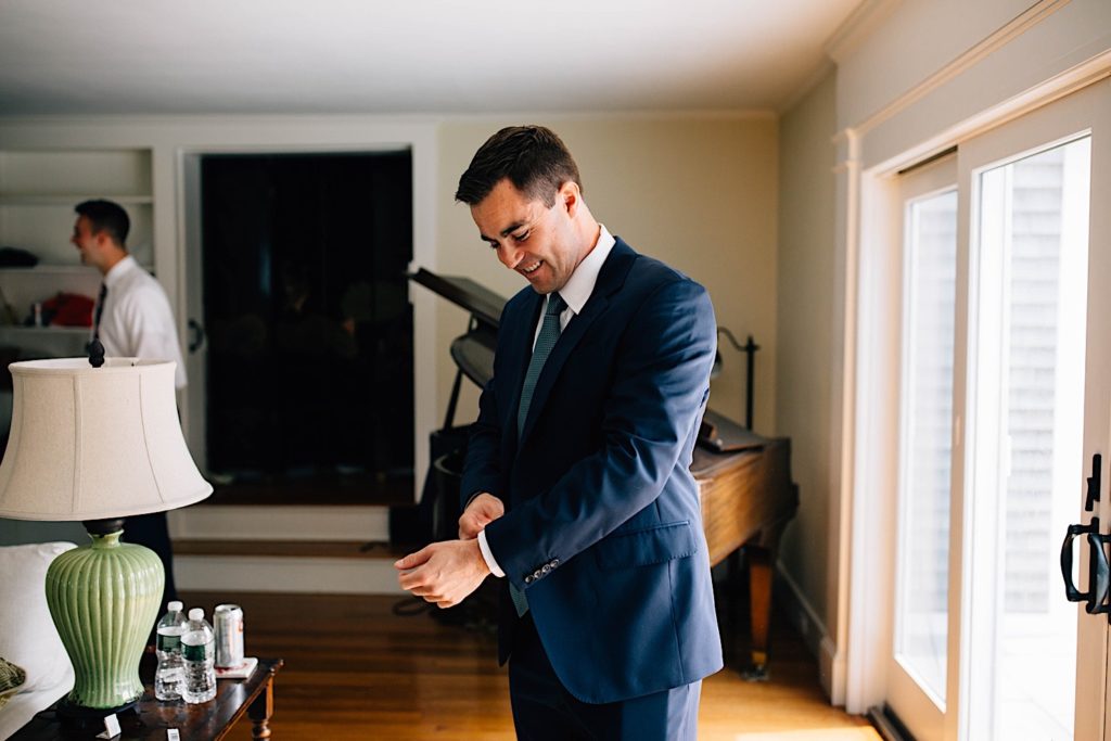 A groom smiles as he adjusts the cuffs on his suit as he gets ready for his wedding day.