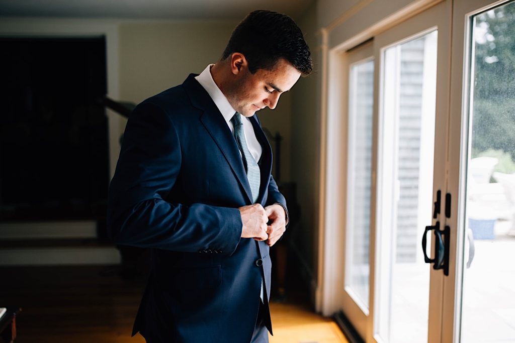 A groom buttons up his suit jacket as he gets ready for his wedding.