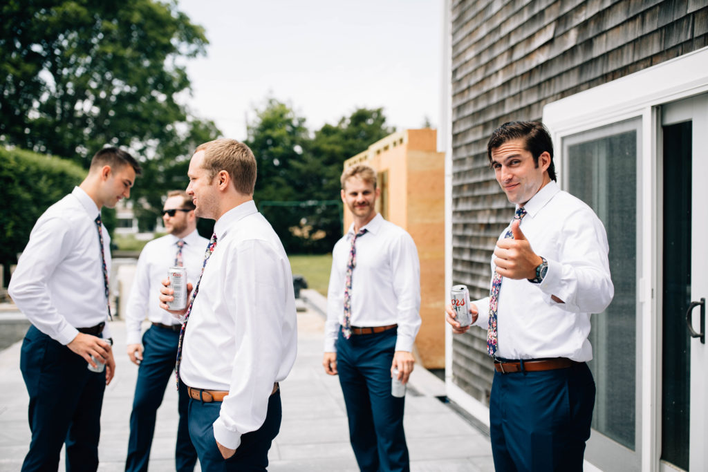 Groomsmen standing outside a house wearing matching dress pants, shirts and ties. They each have a Coors Light in their hand and one man gives the camera a thumbs up.