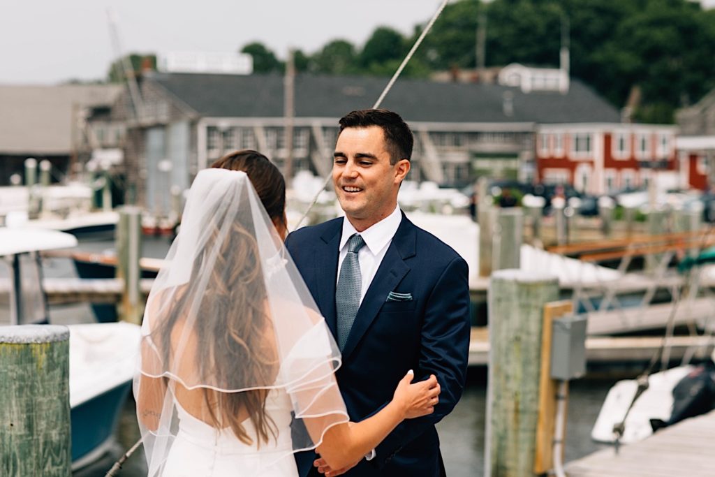 A bride and groom share their first look outside their Cape Cod wedding venue, the bride's back is turned to the camera and the groom is smiling