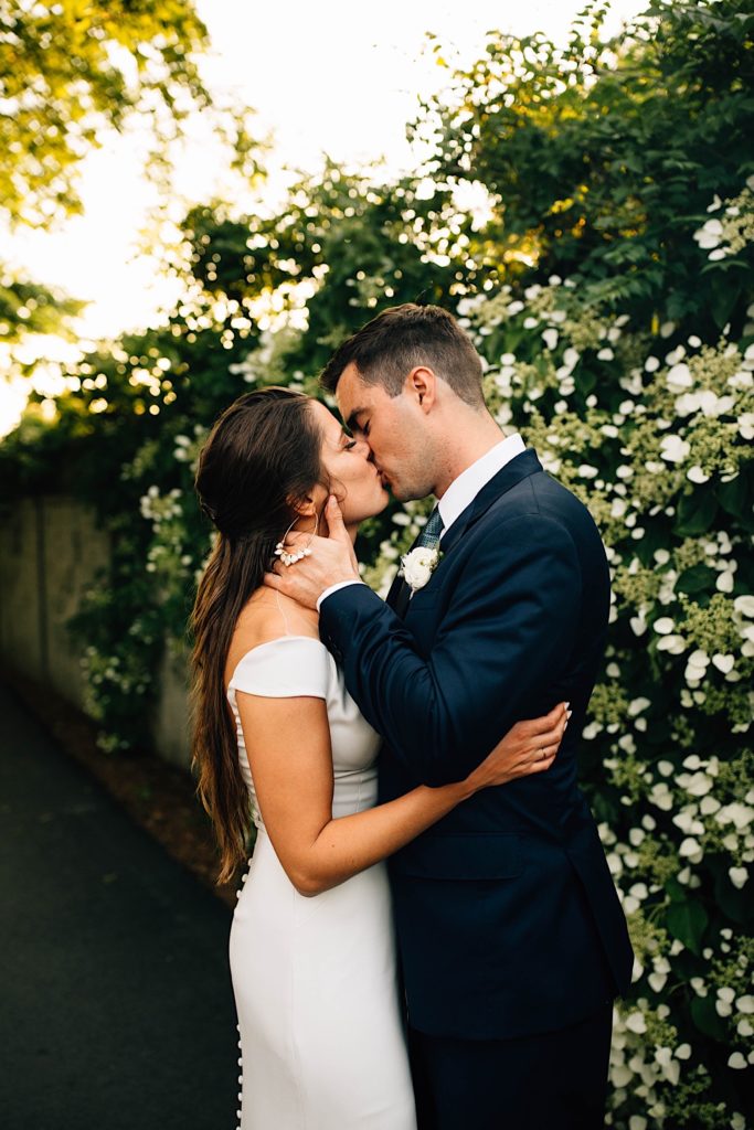 A bride and groom embrace and kiss one another while wearing their wedding attire