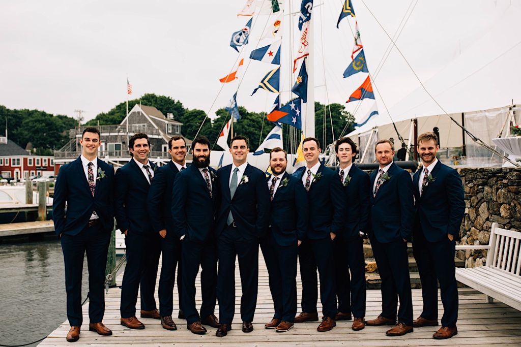 A groom and his groomsmen all stand together on a dock in Cape Cod dressed for the groom's wedding.
