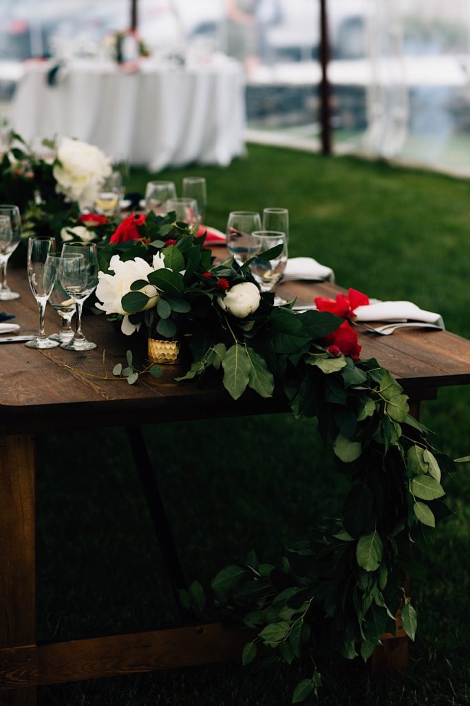 The end of a wooden table that is decorated with flowers for a wedding reception.