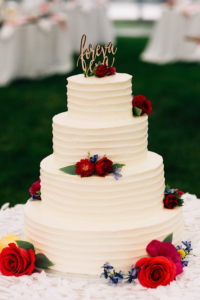 A white wedding cake with 4 levels decorated with red flowers 
